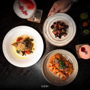 ภาพมุมบนของเมนูอาหารไฟน์ไดนิ่งจาก Davin Cafe ประกอบด้วยเนื้อย่าง ปลาในซอสครีม พาสต้ากุ้ง และค็อกเทลซิกเนเจอร์ บนโต๊ะไม้สีเข้ม