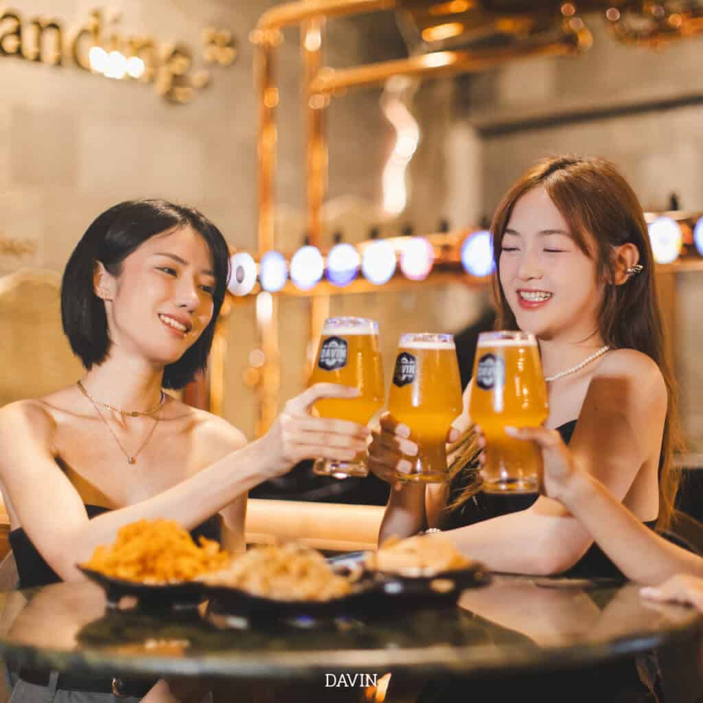 Two women toasting with glasses of Davin craft beer and enjoying fried food at a bar.