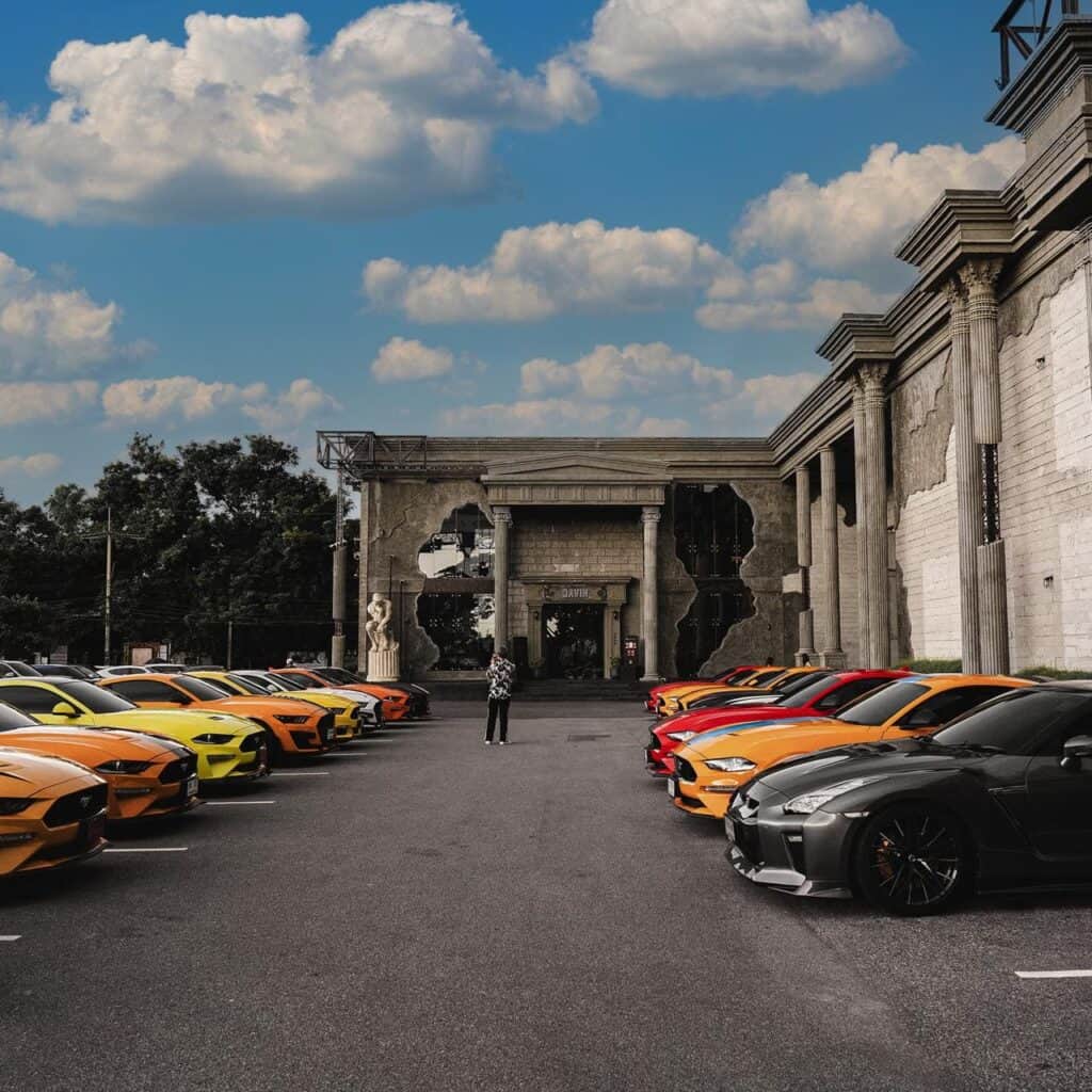 Rows of colorful sports cars, including Ford Mustangs and a Nissan GT-R, parked in front of the Davin building.
