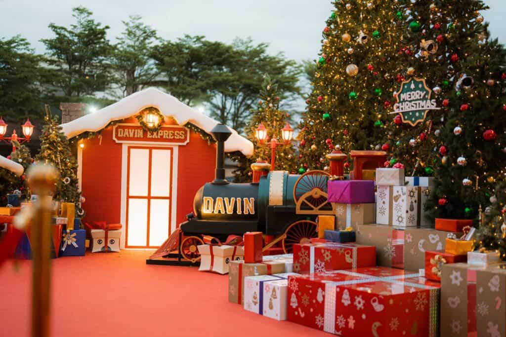 The main Christmas photo spot at Davin Cafe, featuring the miniature "Davin Express" train setup, a festive red house, and large Christmas trees.