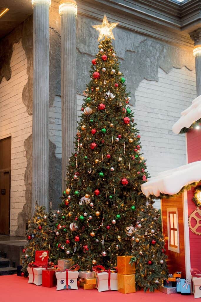 A massive, traditional Christmas tree fully decorated with lights and ornaments, surrounded by gifts, standing between the classical columns of Davin Cafe.