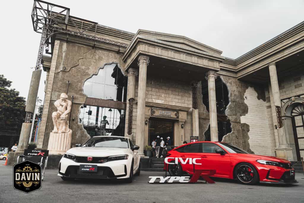 Two new Honda Civic Type R cars (white and red) displayed in front of the spectacular brutalist-classical facade of the Davin Cafe event venue.