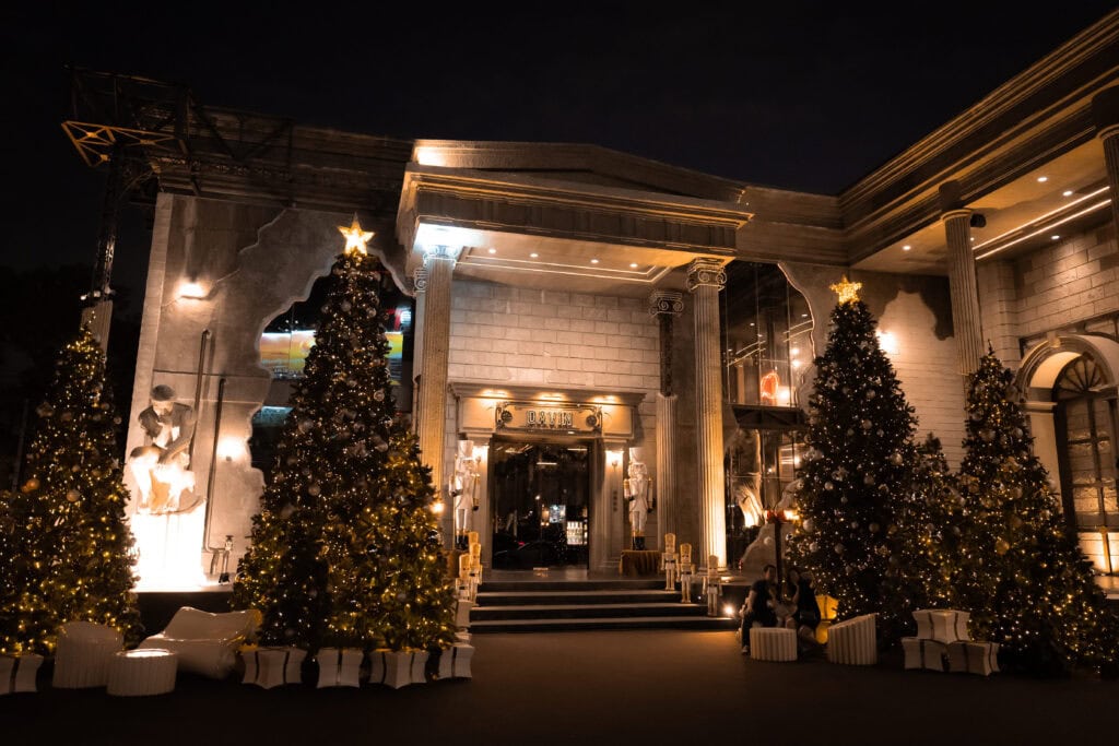 A grand nighttime entrance decorated for Christmas 2025, featuring illuminated Christmas trees, warm festive lighting, and classic architecture, presenting a premium venue setting for Christmas celebrations, year-end events, and elegant holiday gatherings