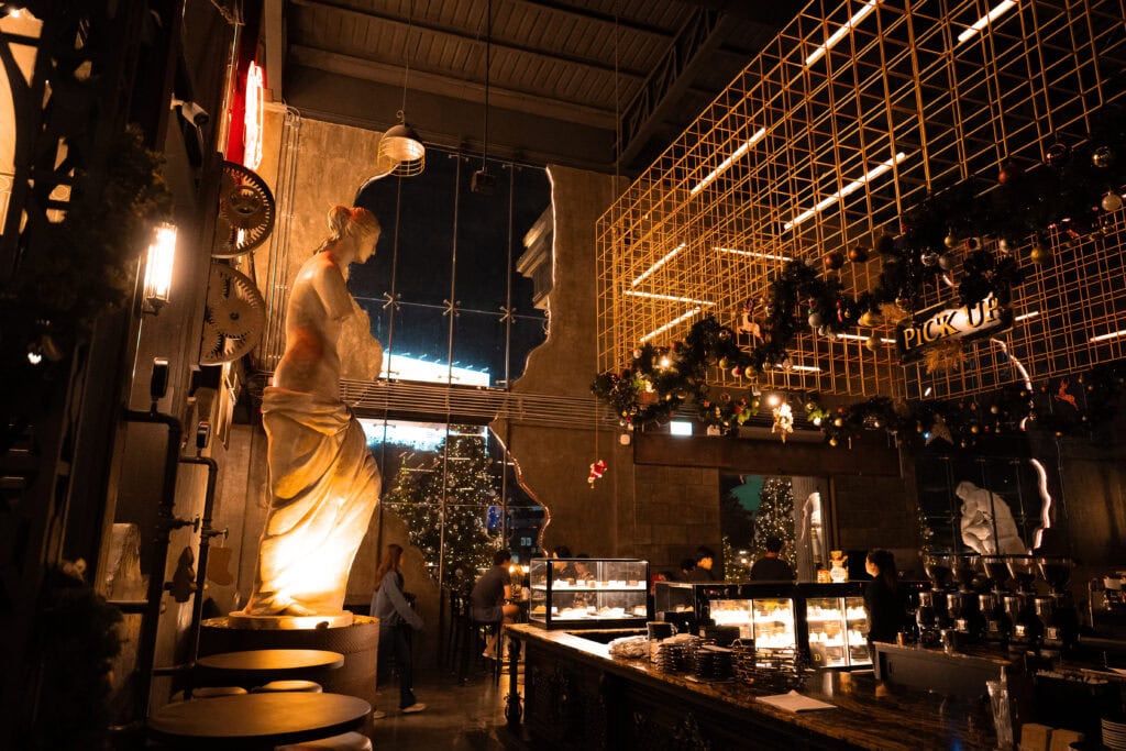 An industrial bar–style event venue interior designed for Christmas 2025, featuring classical sculptures, golden metal structures, and festive lighting, ideal for distinctive Christmas parties and upscale year-end celebrations