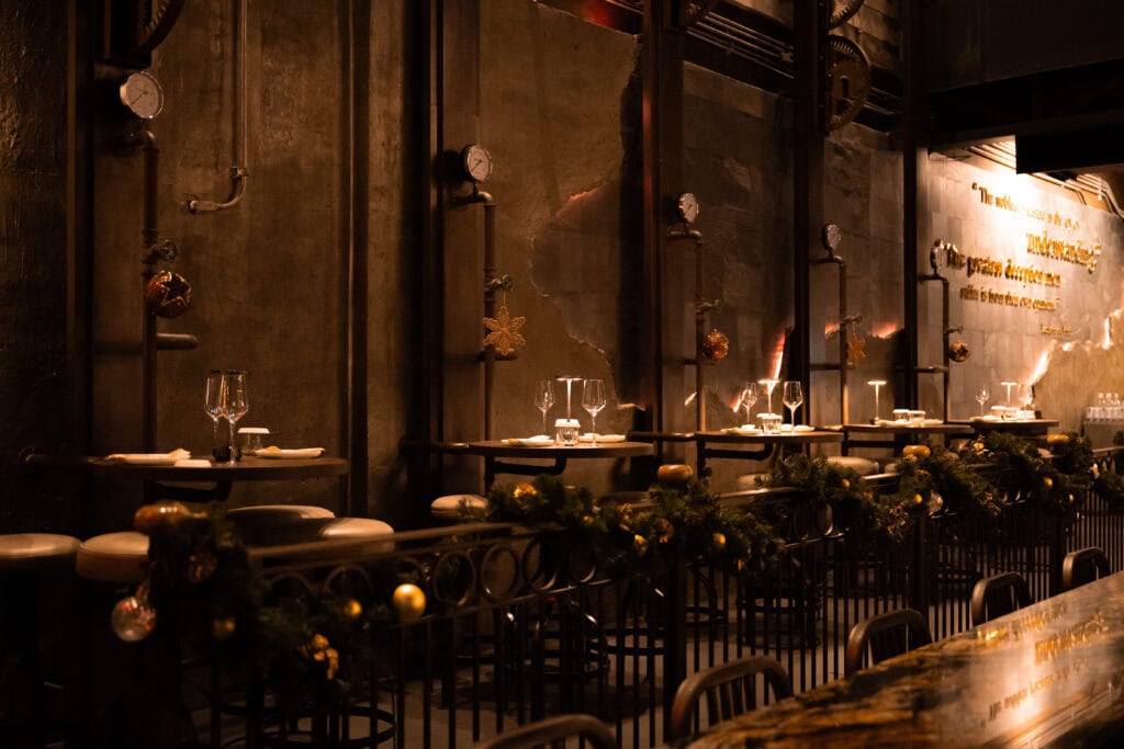 An industrial-style dining space designed for Christmas 2025, featuring warm ambient lighting, raw steel elements, and an elegant dinner setup, ideal for exclusive Christmas parties and premium year-end celebrations