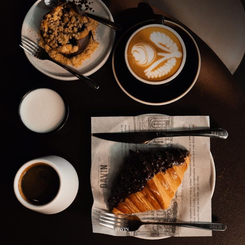 Artisan bakery croissant served with coffee, featuring latte art and espresso in a real café setting