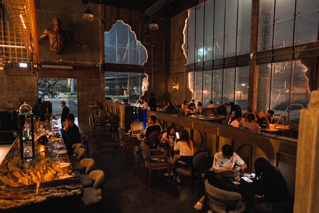 บรรยากาศภายในคาเฟ่รามอินทราช่วงเย็น ลูกค้านั่งทานอาหาร พูดคุย และทำงานในพื้นที่เพดานสูง กระจกบานใหญ่ และแสงไฟอุ่นของ Davin Cafe ที่เหมาะทั้งนัดพบและดินเนอร์ยามค่ำคืน