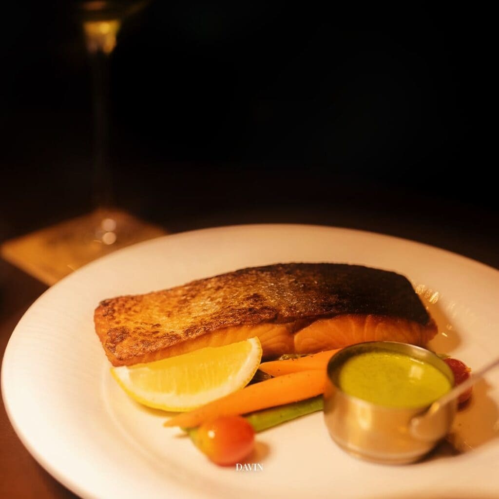 Grilled salmon dinner served in a night hangout restaurant, warm ambiance ideal for relaxed dining, social gatherings, and evening hangout experiences