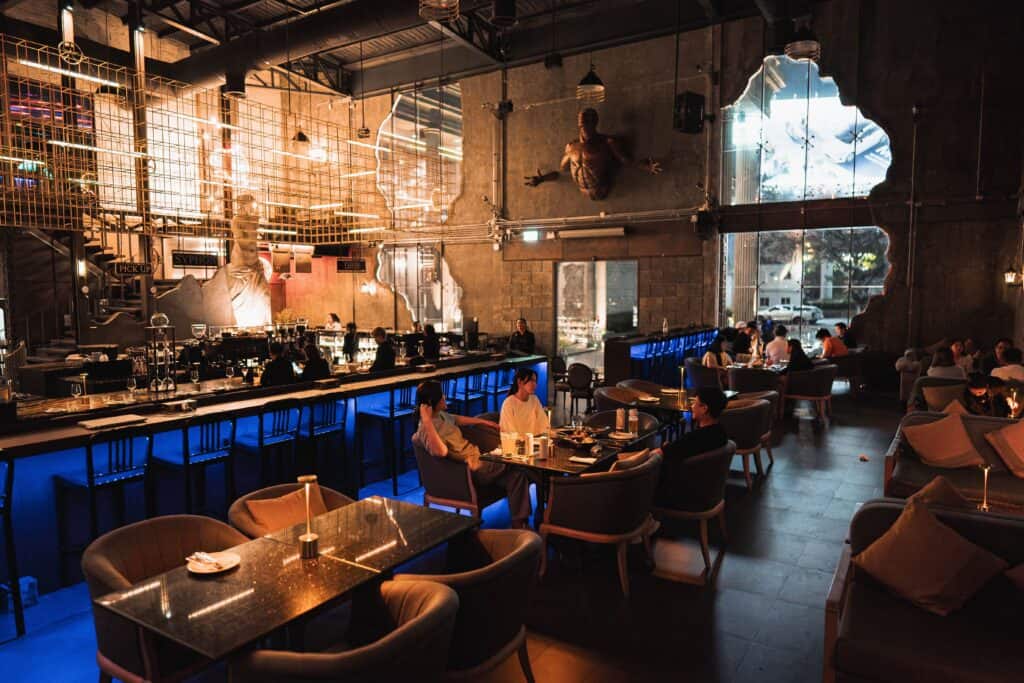 Premium night hangout with an industrial-style bar and dining area, people enjoying dinner, drinks, and relaxed conversations in an evening social atmosphere