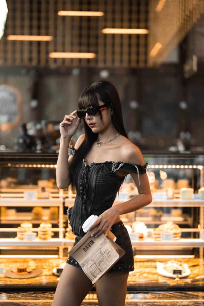 A fashion-forward lifestyle moment inside Davin Cafe, a cafe along the Ramintra Expressway, where a guest poses in front of the pastry display, reflecting a premium café atmosphere designed for style, social moments, and visual storytelling.