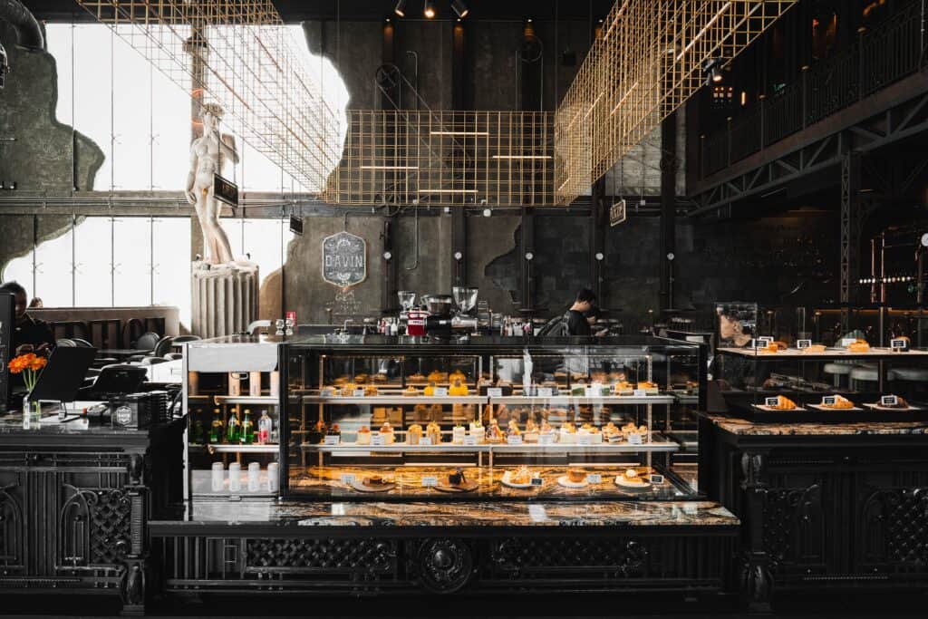 บรรยากาศภายใน Davin Cafe พร้อมเคาน์เตอร์ตู้กระจกโชว์ขนมอบและเค้กโฮมเมดหลากหลายชนิด ใจกลางร้านสไตล์อินดัสเทรียลหรู สะท้อนภาพลักษณ์ของ bakery bangkok ที่ผสานงานดีไซน์ ประสบการณ์ และคุณภาพสินค้าไว้ในพื้นที่เดียว