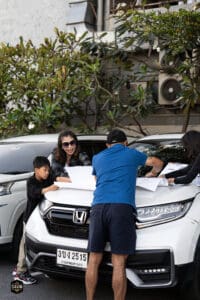 รถยนต์ Honda จอดหน้าร้านกาแฟ Davin Cafe พร้อมผู้คนกำลังดูแผนที่และสนทนาในบรรยากาศกลางแจ้ง.