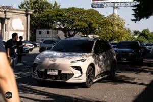 รถยนต์ไฟฟ้าสีขาวจอดอยู่ในลานจอดรถหน้าร้าน Davin Cafe บรรยากาศกลางแจ้งในวันที่มีแดดและต้นไม้เขียวขจีใ.