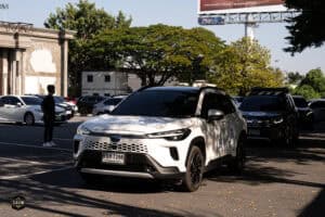 รถยนต์ไฟฟ้าสีขาวจอดในลานจอดรถที่ Davin Cafe พร้อมฉากธรรมชาติและป้ายโฆษณาในพื้นหลัง.