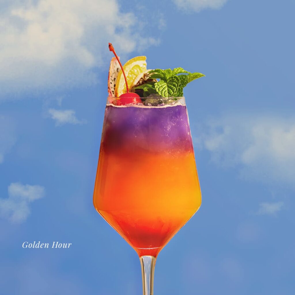 A wide shot of the exclusive Davin Cafe summer menu experience on Pradit Manutham Road, featuring a complete set of seafood main course, vibrant cocktails, and coconut dessert beautifully arranged on a beach sand display.