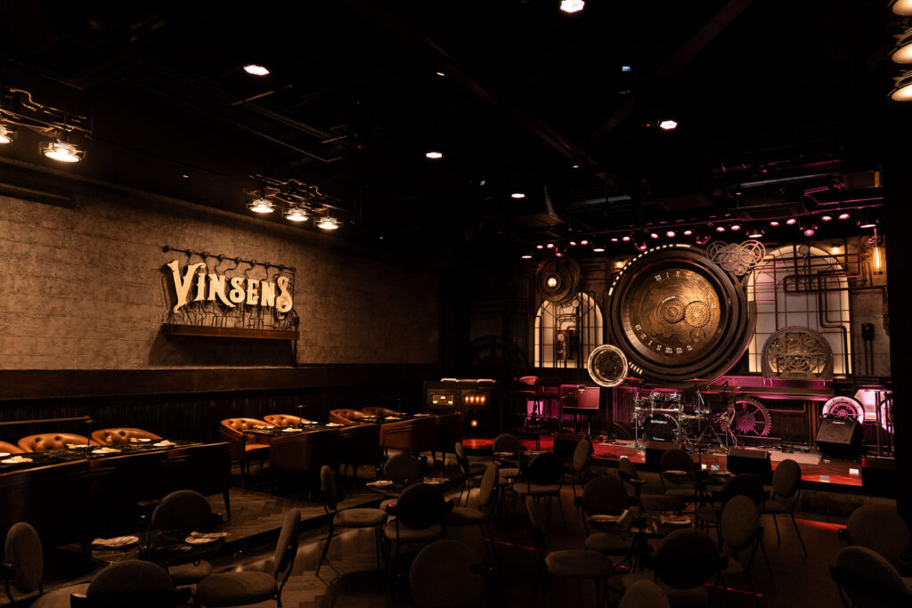 Wide-angle interior of Vinsens, a premium chill bar in Ramintra, showcasing its industrial-style live music stage, ambient lighting, and upscale seating designed for immersive nightlife experiences