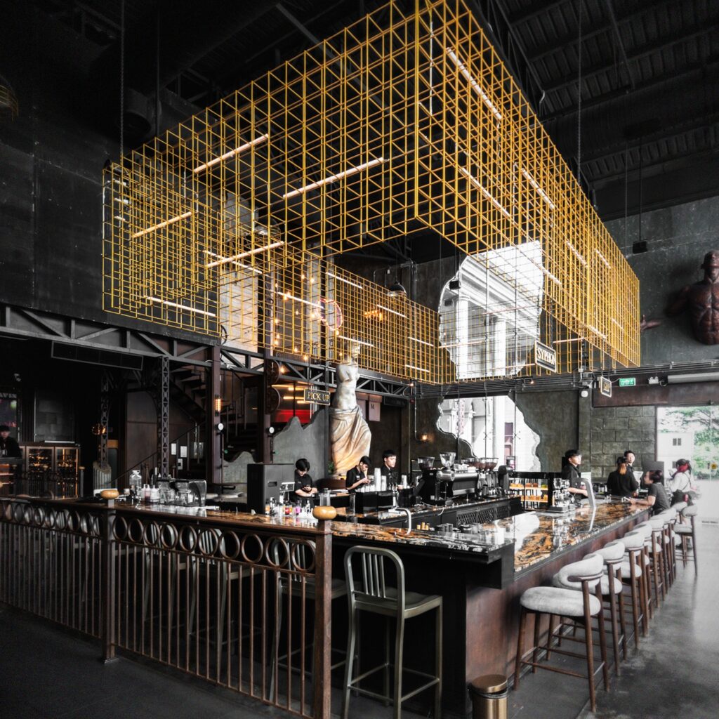 Grand bar interior at Davin Cafe, a European-style cafe in Bangkok featuring a marble counter, dramatic high ceiling, classical sculptures, and industrial luxury details that create a distinctive coffee and dining destination.