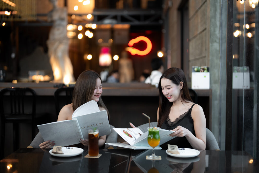 ลูกค้ากำลังเลือกเมนูเครื่องดื่มภายใน Davin Cafe ร้านคาเฟ่สไตล์ ยุโรปในกรุงเทพ ที่มีบรรยากาศหรู อบอุ่น และเหมาะสำหรับนั่งพักผ่อนกับเพื่อน พร้อมมุมถ่ายรูปสวยและเครื่องดื่มซิกเนเจอร์ที่ช่วยเติมเต็มประสบการณ์คาเฟ่