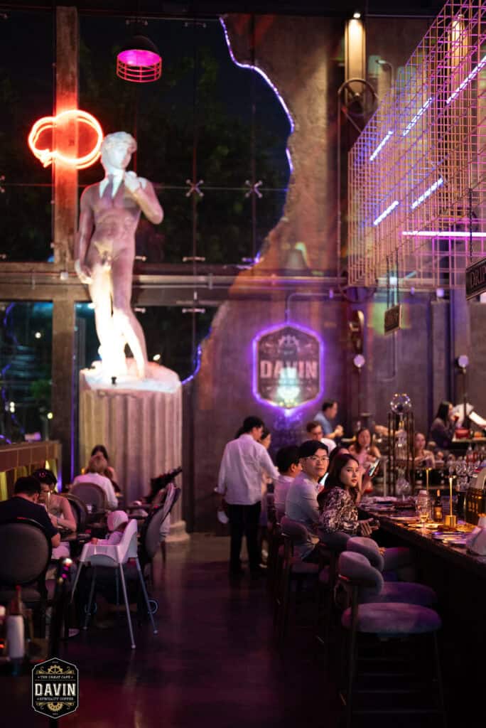 Evening event atmosphere inside Davin Cafe with guests seated around the bar and dining area, highlighting a Bangkok fan meet venue with dramatic lighting, distinctive interiors, food and beverage service, and flexible space for artist gatherings, fan activities, and private events.
