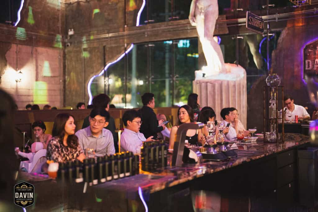 Guests enjoying drinks and conversations around the bar at Davin Cafe, showcasing a premium Bangkok fan meet venue with atmospheric lighting, flexible seating, photo-friendly interiors, and full food and beverage service for fan gatherings and private events.