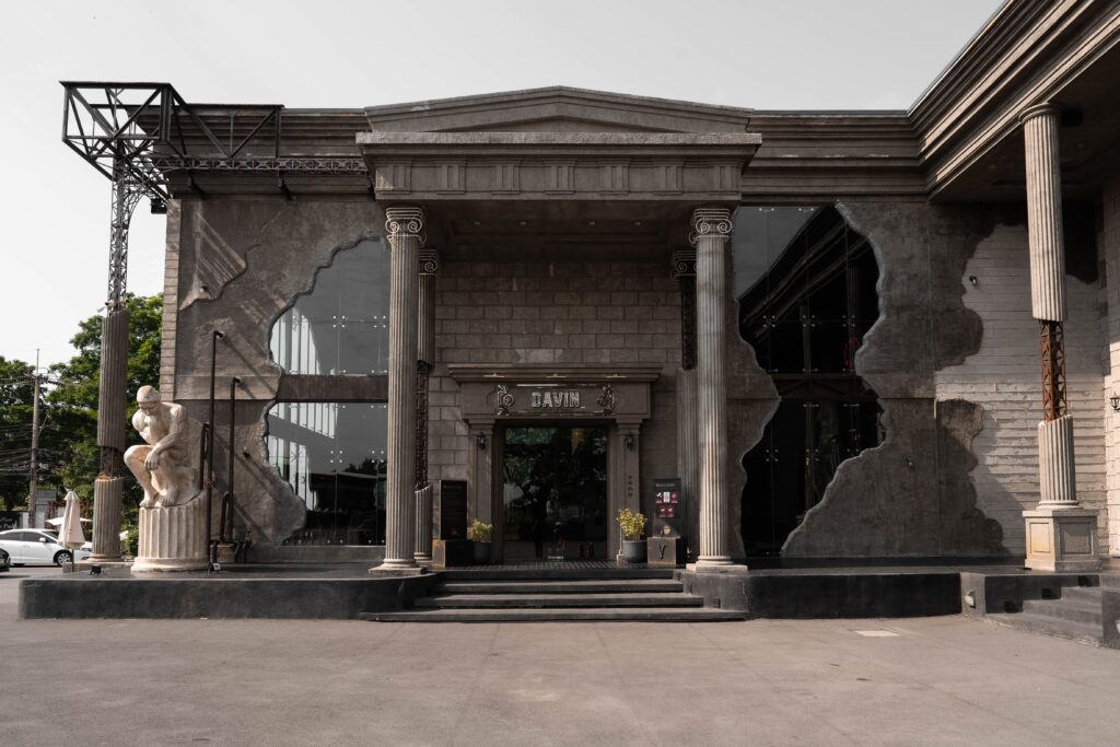 ด้านหน้า Davin Cafe ร้านคาเฟ่สไตล์ ยุโรปในกรุงเทพ ที่โดดเด่นด้วยเสาโรมัน ประติมากรรมคลาสสิก และสถาปัตยกรรมขนาดใหญ่ ให้บรรยากาศเหมือนได้เช็กอินคาเฟ่ต่างประเทศตั้งแต่ก่อนเดินเข้าร้าน