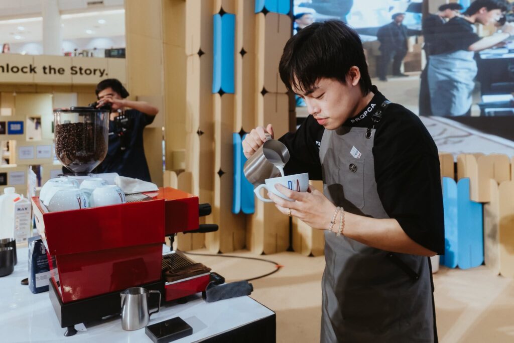 DAVIN CAFE barista competing on stage at PCA Latte Art Thailand 2026, demonstrating precision milk pouring, specialty coffee expertise, and professional latte art competition skills alongside advanced coffee equipment