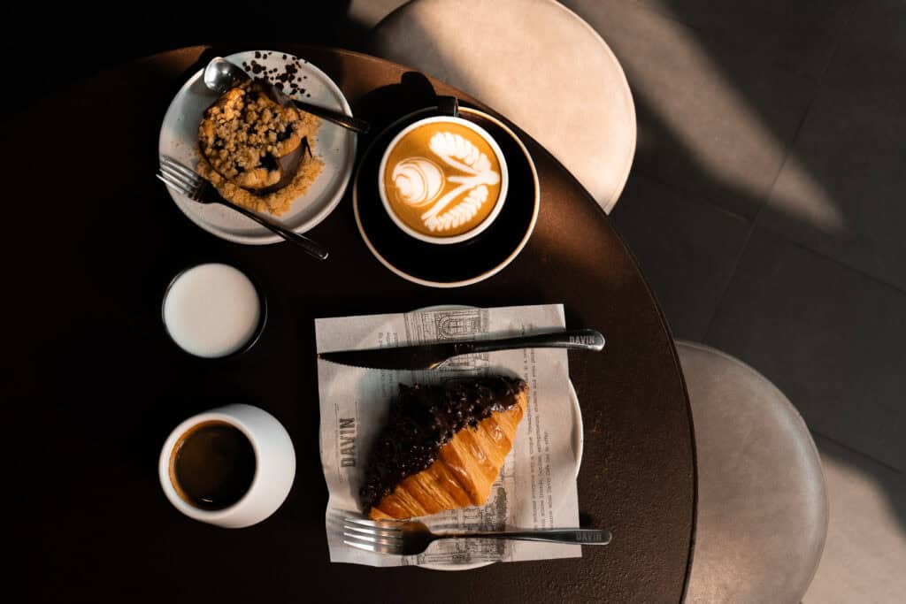 Coffee and dessert pairing table at Davin Cafe with latte art, espresso, chocolate croissant, and baked pastry in warm natural light, reflecting the Flavor Exchange concept through thoughtful taste pairing and a refined cafe experience.