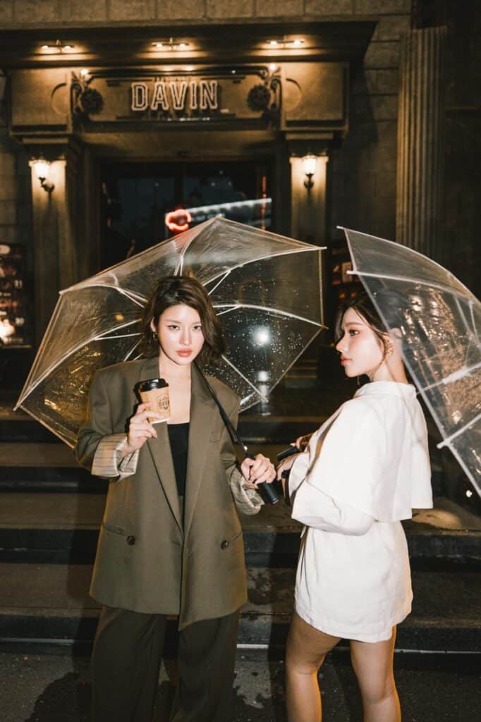 ไอเดียท่าโพสถ่ายรูปคาเฟ่รับหน้าฝนของสองสาวถือร่มใสและแก้วกาแฟ บริเวณทางเข้า DAVIN CAFE รามอินทรา ในลุคแฟชั่นสไตล์นิตยสาร